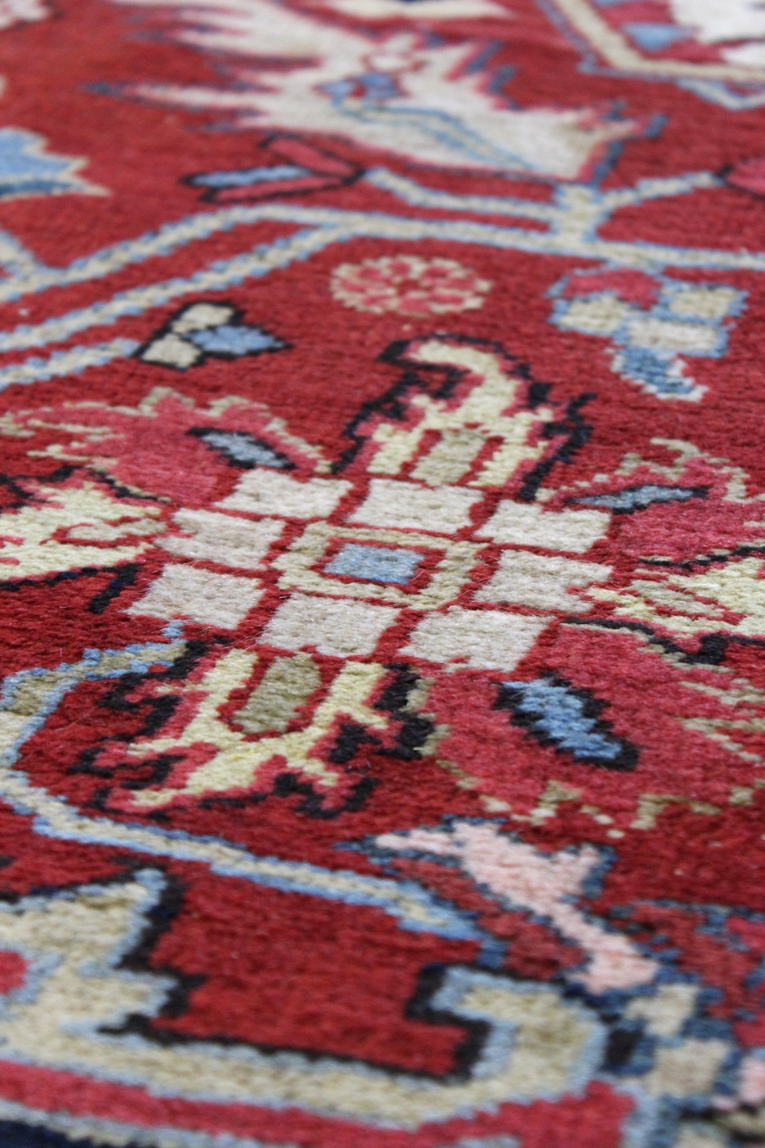 Close-up detail of a handwoven rug's intricate, red and beige pattern.
