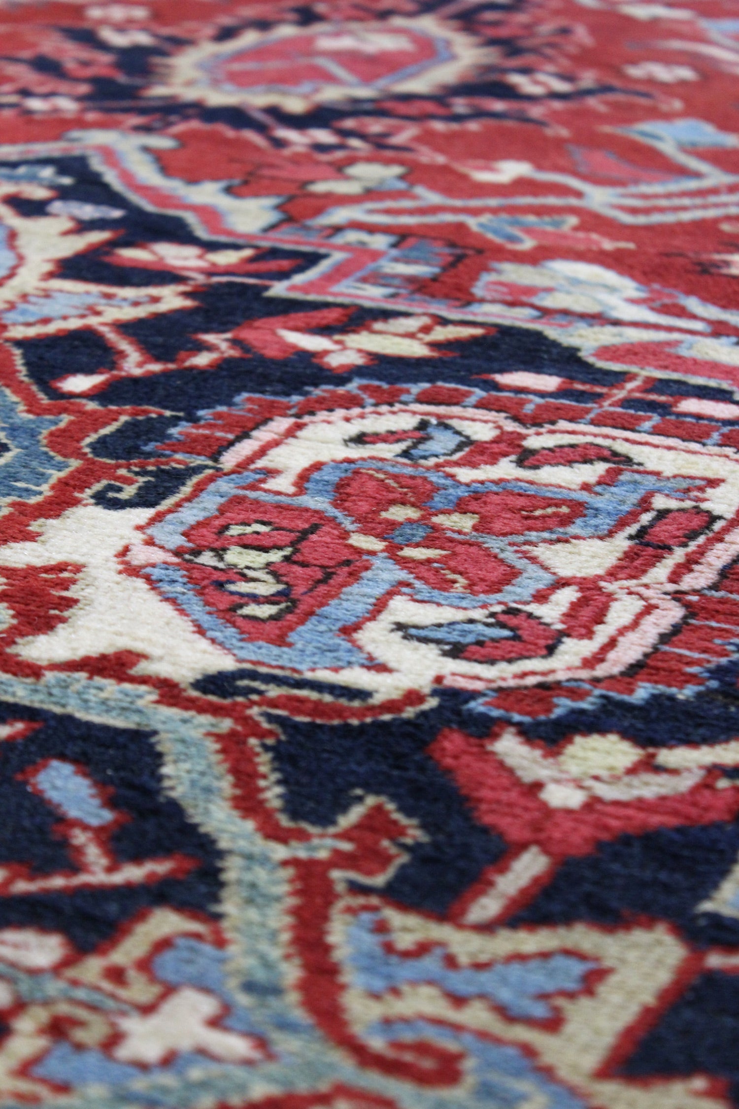 Close-up of a handwoven rug's intricate red, blue, and cream pattern.
