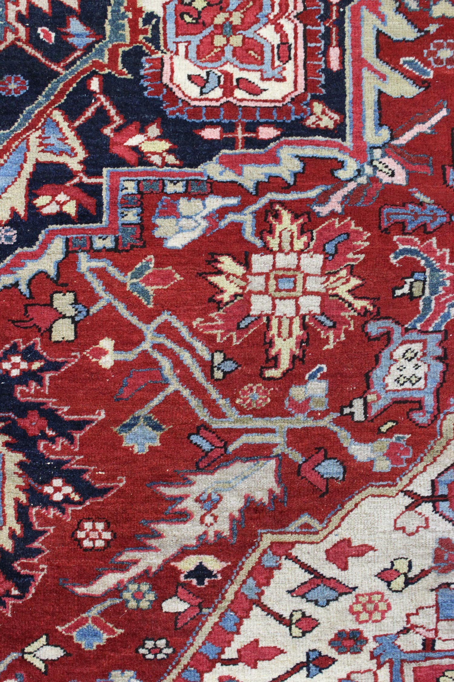 Detail of antique Heriz rug's handwoven floral pattern in red, blue, and beige.
