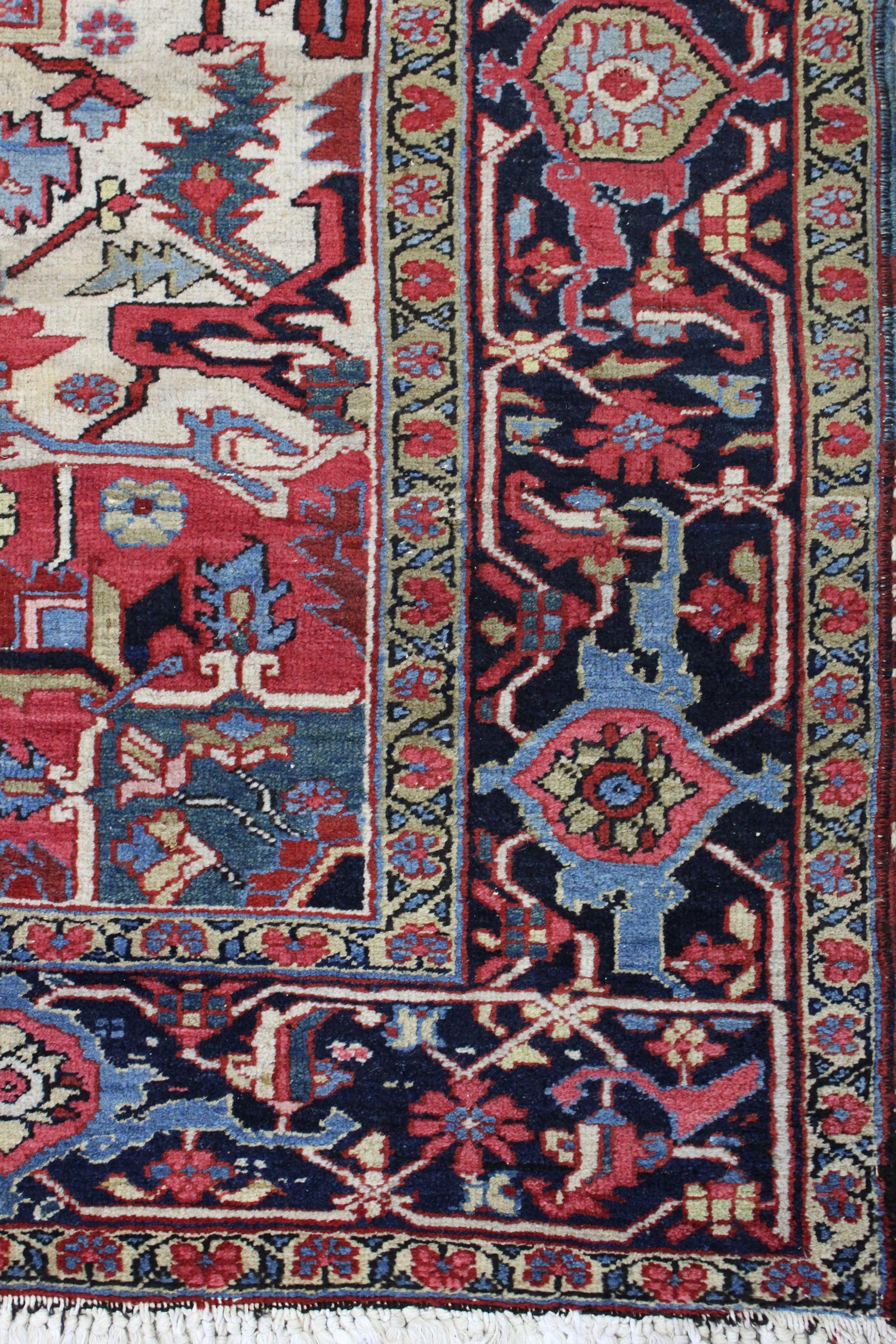 Antique Heriz rug detail: handwoven, vibrant red, blue, and ivory floral pattern with intricate border.
