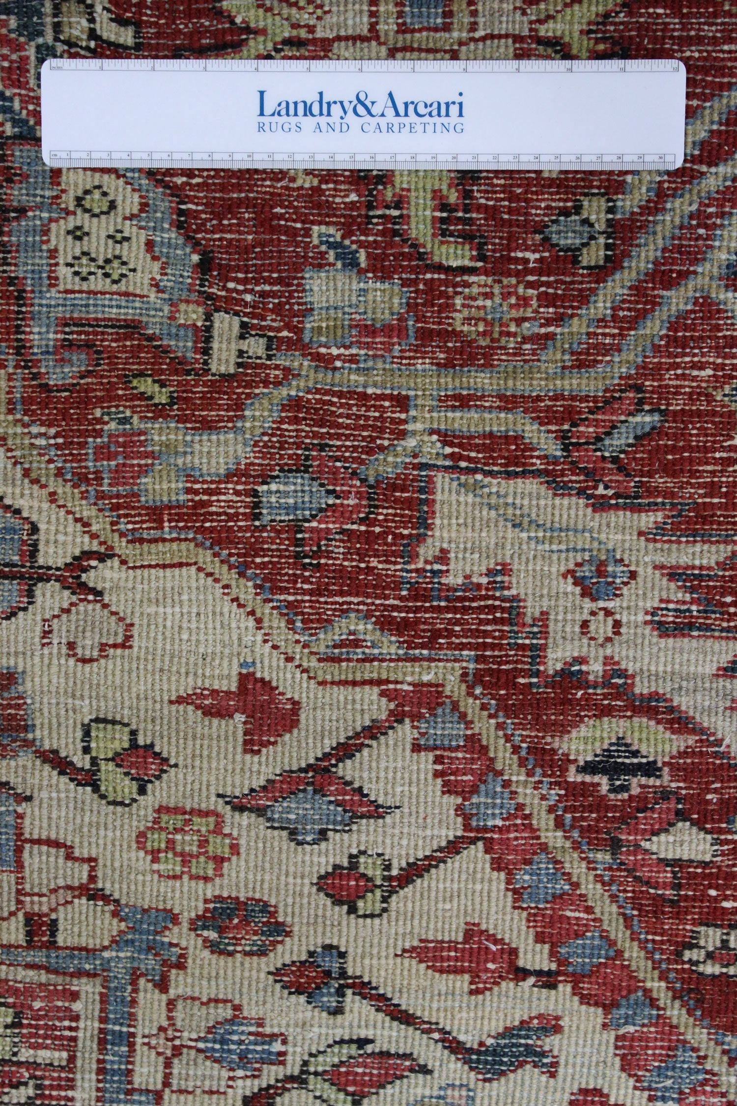 Close-up detail of antique Heriz rug's handwoven texture, showcasing red, beige, and blue tones.
