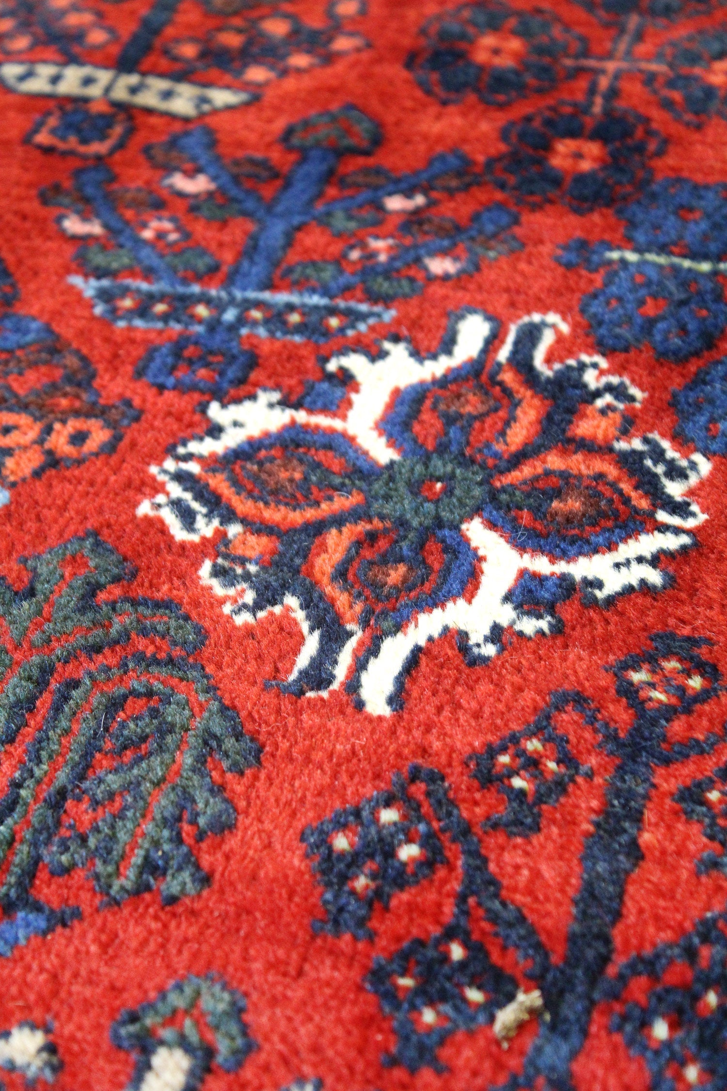 Close-up of red handwoven rug detail, intricate navy and cream pattern.
