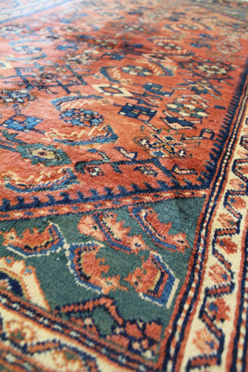 Handwoven rug detail:  Intricate orange, teal, and navy pattern in antique tribal design.
