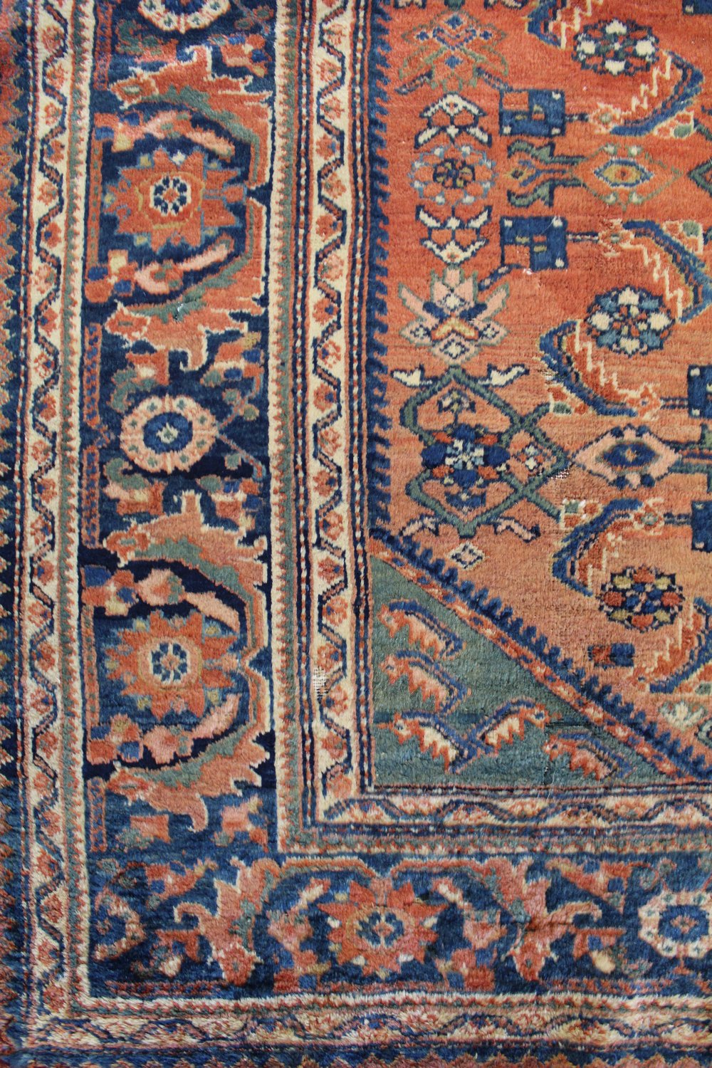 Detailed close-up of an antique rug's intricate, handwoven pattern in shades of blue, red, and cream.
