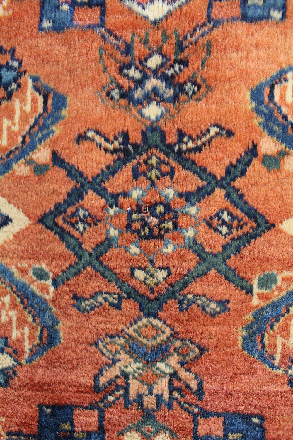 Close-up of an antique rug's handwoven, rust-toned pattern with dark blue and cream accents.
