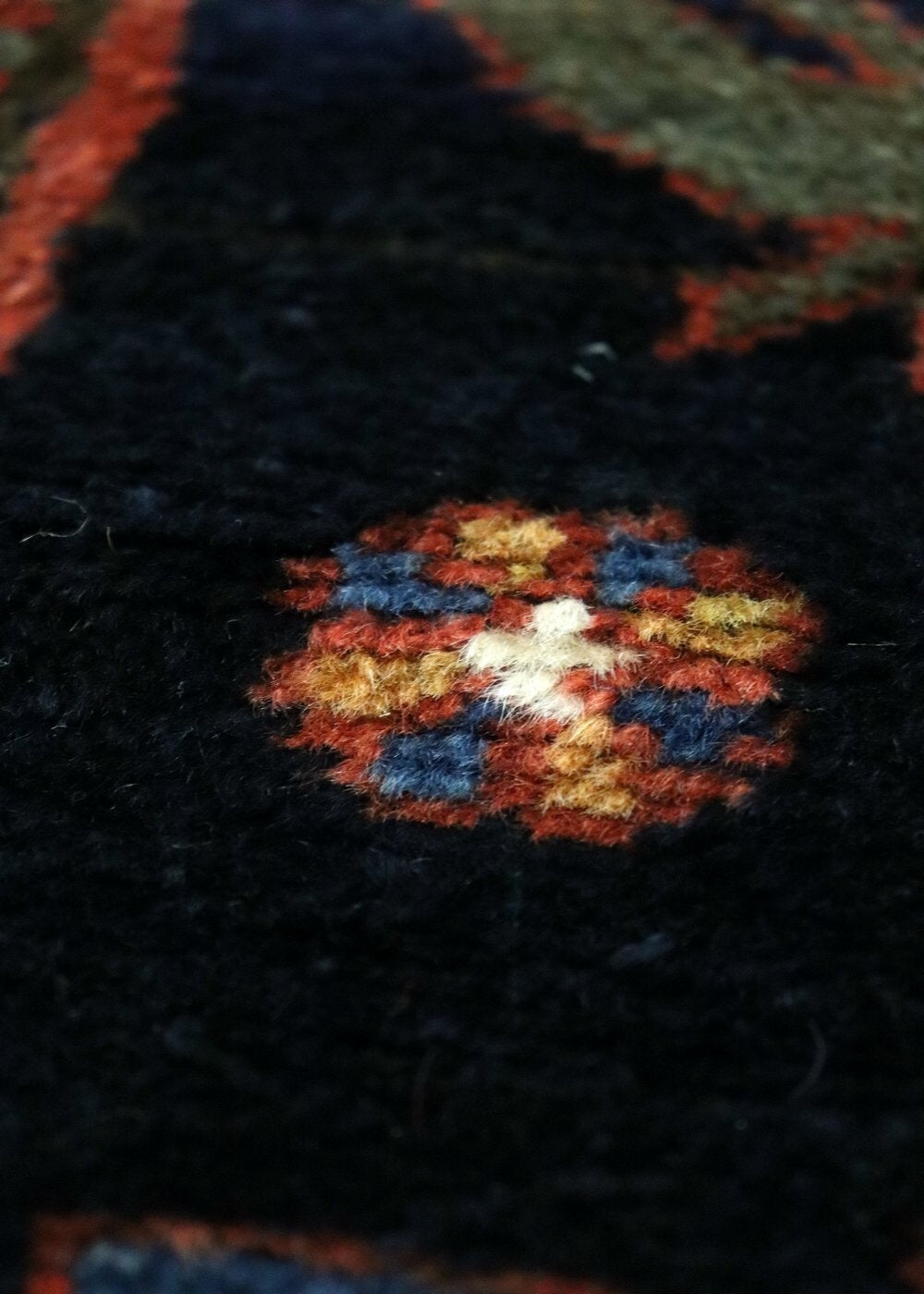 Close-up detail of handwoven rug, showcasing intricate multicolored floral pattern on dark background.
