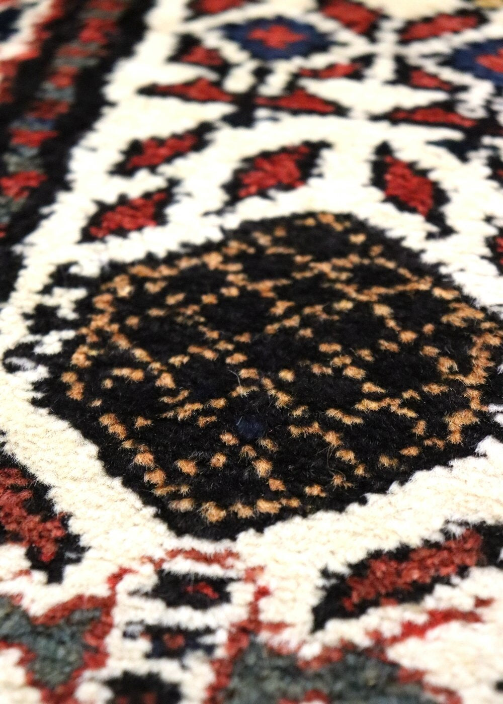 Close-up detail of a handwoven rug's intricate, black and red pattern on an off-white background.
