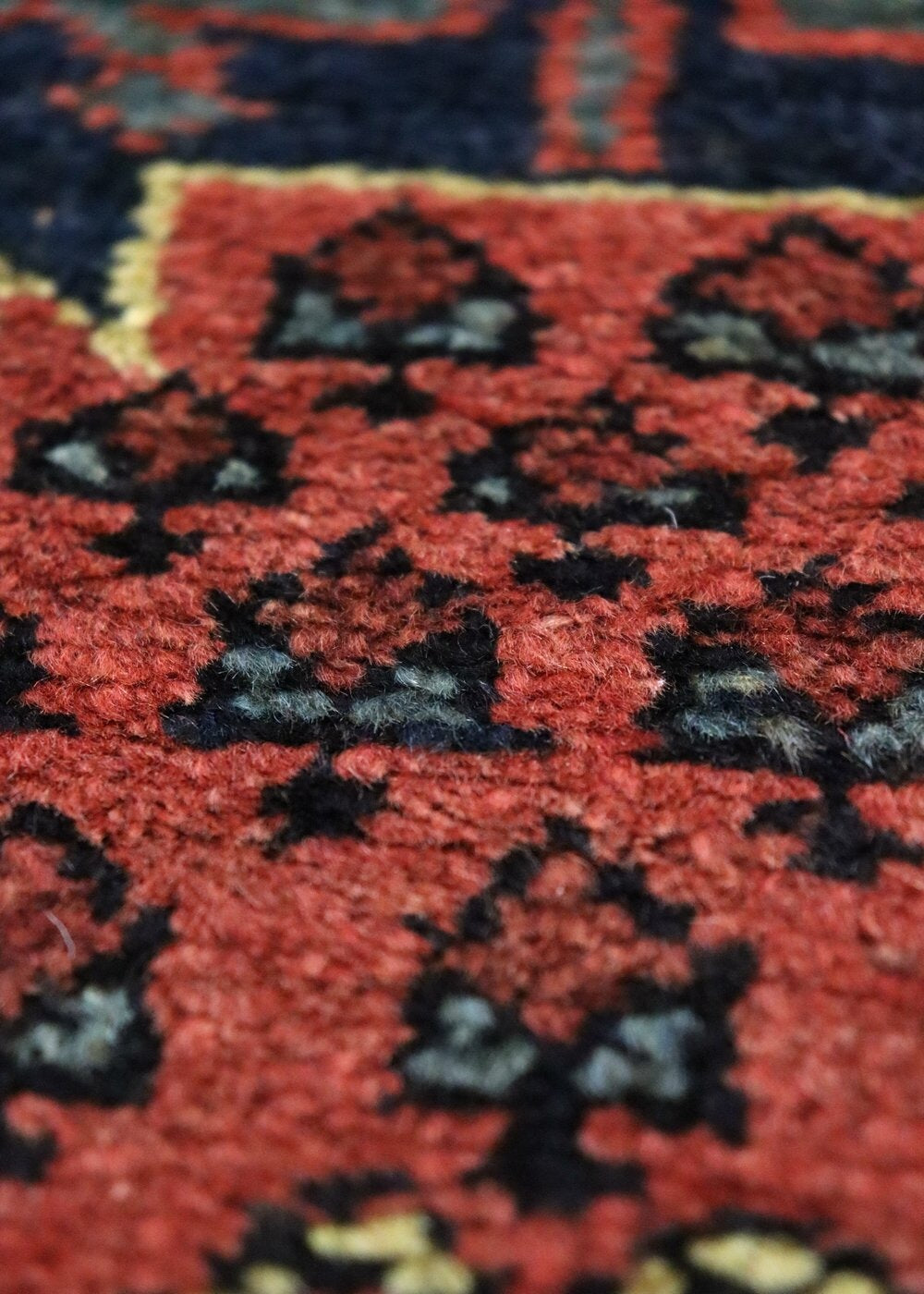 Close-up of richly colored handwoven rug detail, showcasing intricate red and black tribal pattern.
