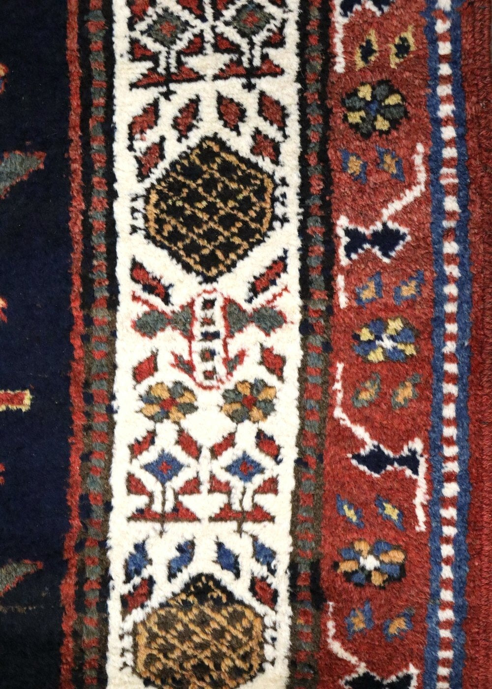 Close-up of handwoven rug detail, showcasing intricate floral and geometric patterns in rich reds, blues, and creams.
