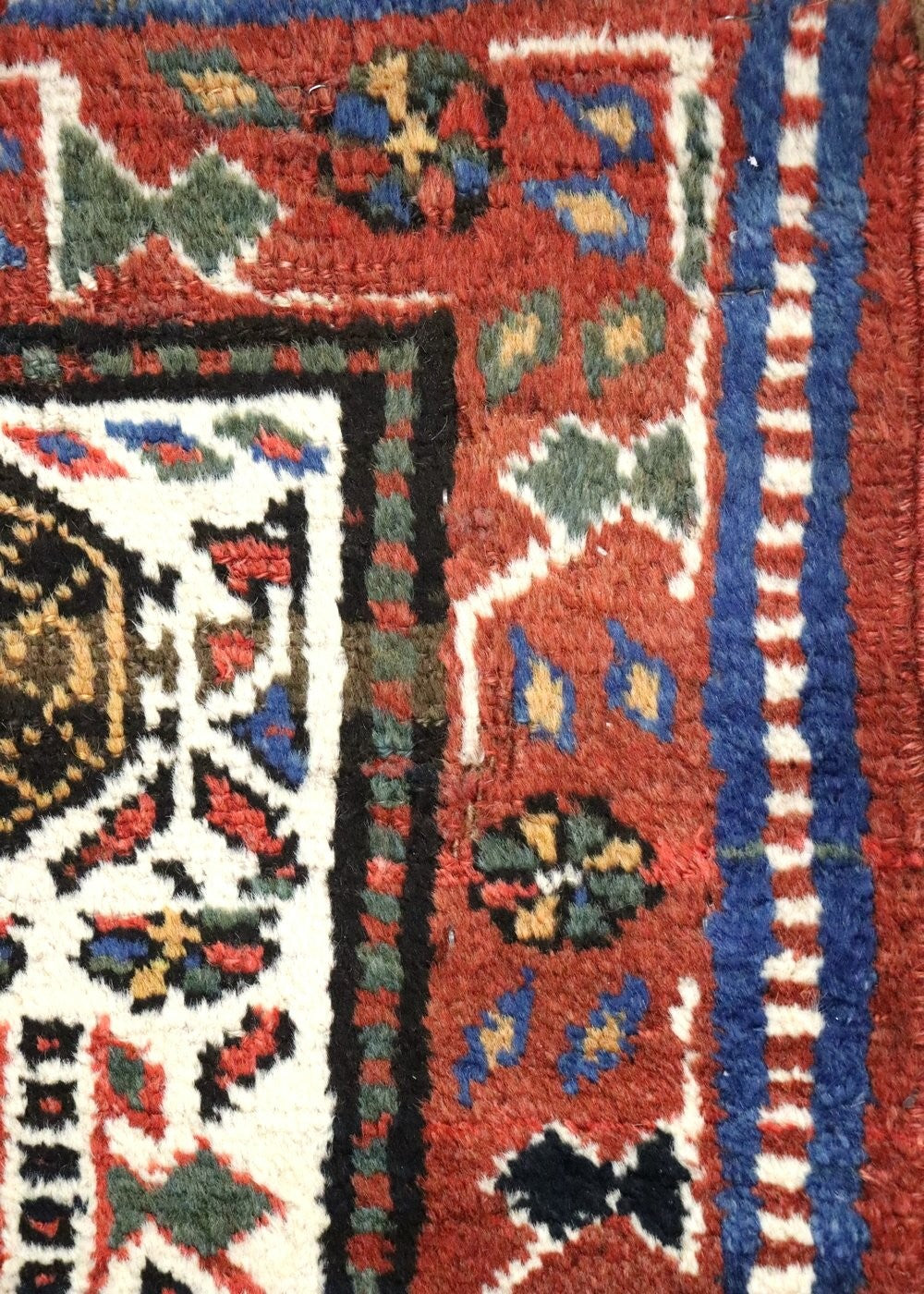 Close-up detail of a handwoven rug's corner, showcasing intricate red, blue, and cream patterns.
