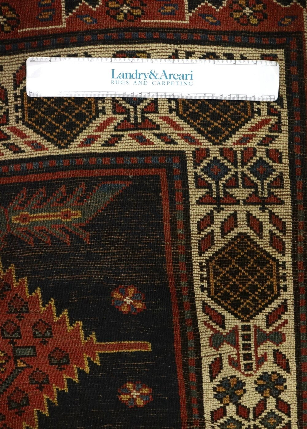 Antique handwoven rug detail, showcasing intricate tribal patterns in red, beige, and dark blue on a black background.
