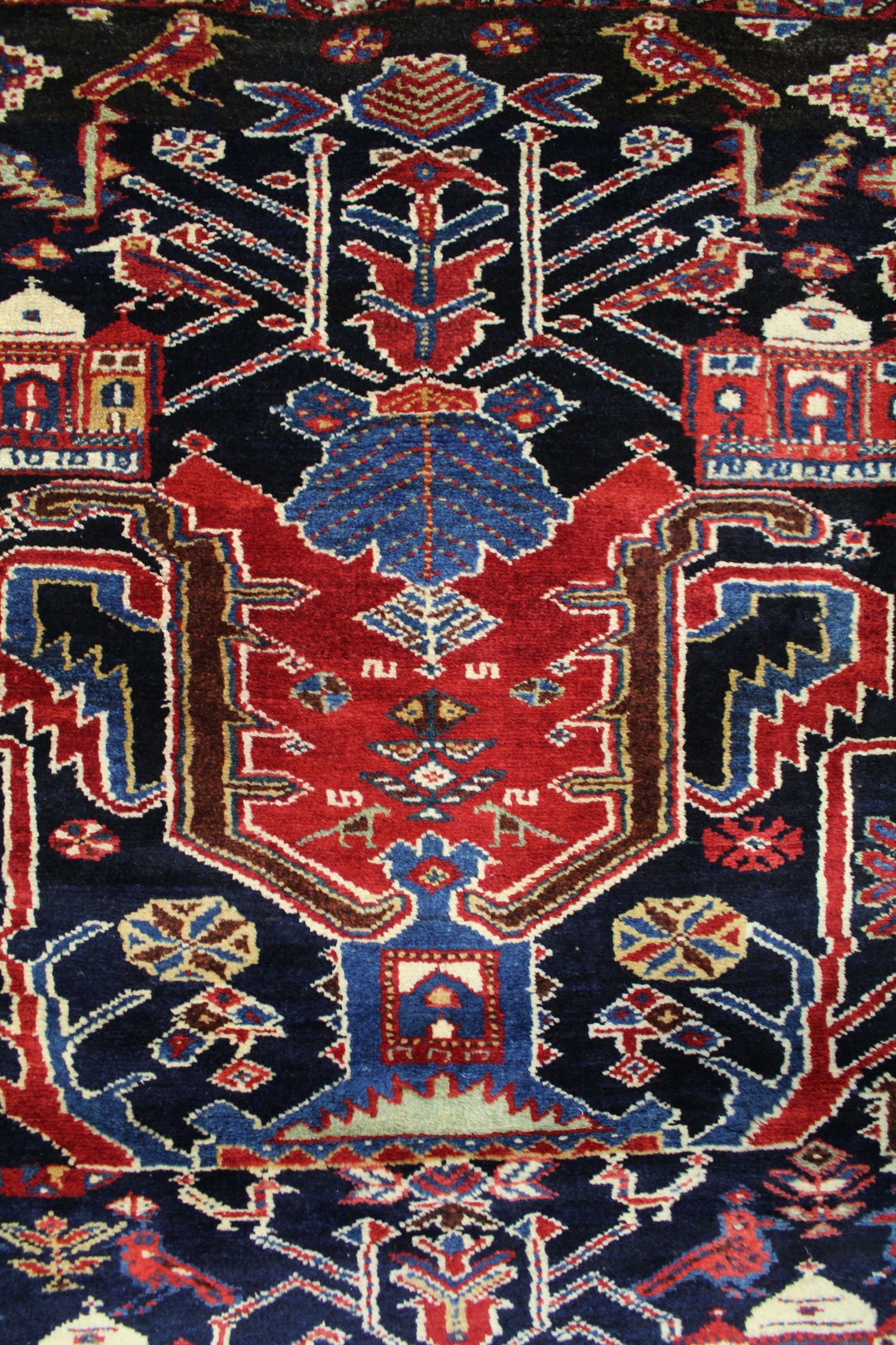 Intricate detail of a handwoven tribal rug, featuring a navy blue base with red, blue, and cream patterns.
