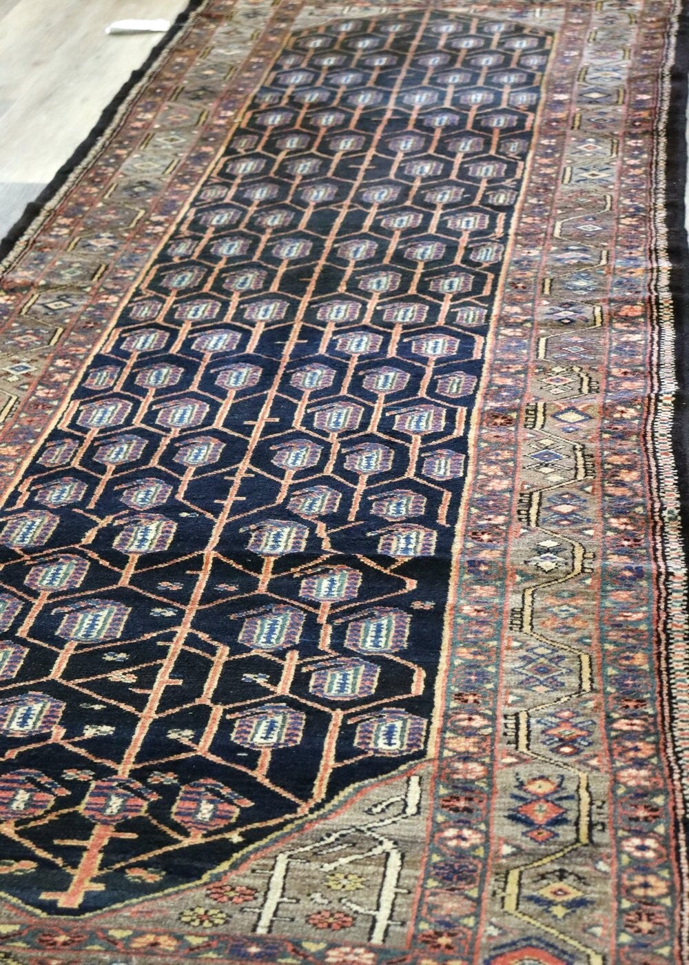 Handwoven tribal rug with a dark background, intricate geometric pattern, and muted floral accents.
