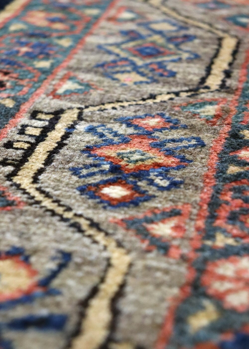 Close-up of antique Malayer rug detail, showcasing handwoven tribal pattern in muted reds, blues, and beige.
