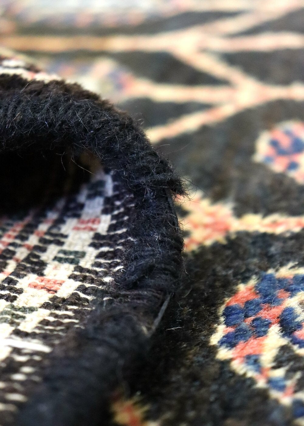 Close-up of handwoven rug detail, showcasing intricate pattern and dark, textured fringe.
