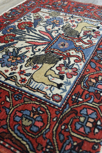 Handwoven tribal rug detail: red border, cream center with lions, birds, and floral motifs.
