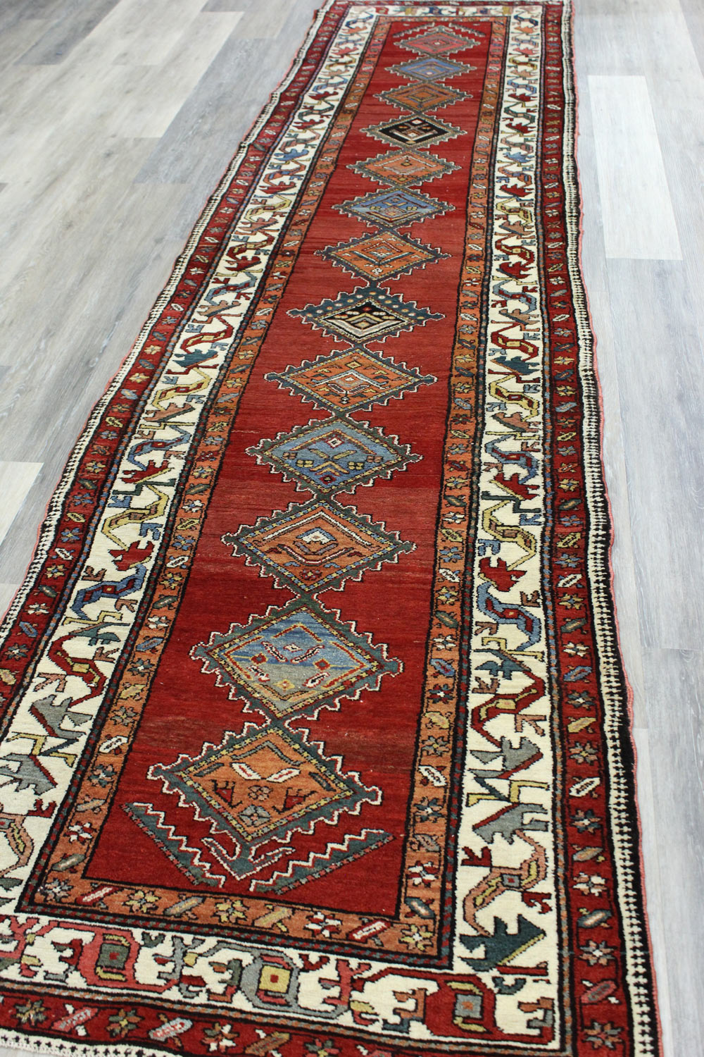 Handwoven tribal rug, red with intricate patterns, displayed on wood floor.
