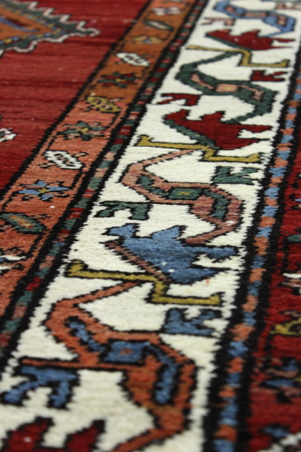 Handwoven rug detail: close-up of intricate tribal pattern in red, cream, and blue.
