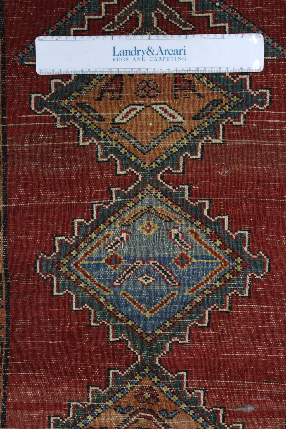 Close-up detail of antique Persian rug's handwoven, geometric pattern in red, blue, and green.
