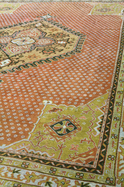 Detail of antique Oushak rug; handwoven, muted orange and green tones, intricate tribal pattern.
